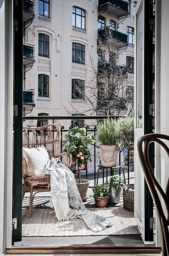 a small balcony with a wicker chair, potted greenery and baskets for storage is a beautiful light-filled space