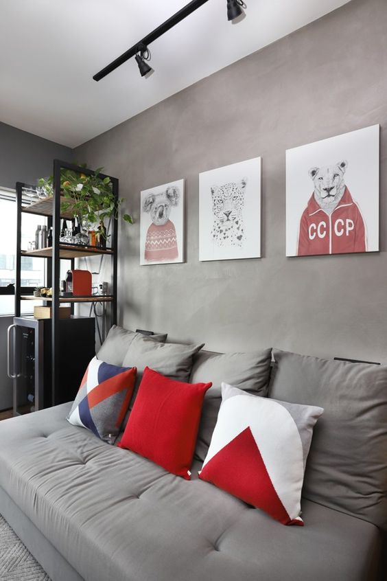 a small industrial living room with grey limewashed walls, a grey sofa with red and navy pillows, a gallery wall with reds