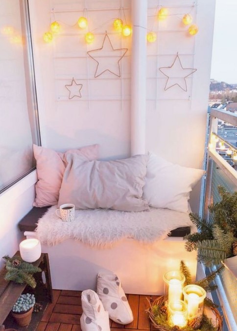 a small winter balcony with lots of lights, star decor, faux fur, pastel pillows, candles, pinecones and evergreens