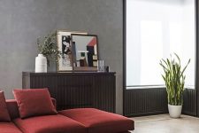 a sophisticated living room with grey limewashed walls, a deep red sectional, a dark-stained sideboard and matching paneling