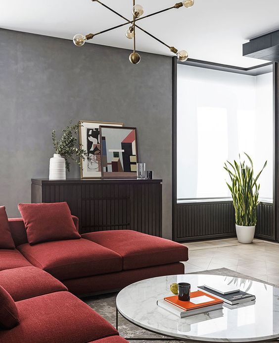 a sophisticated living room with grey limewashed walls, a deep red sectional, a dark stained sideboard and matching paneling