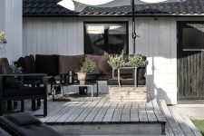 a stylish Scandinavian terrace with a black sofa, chair and loungers, an umbrella and a coffee table is all cool