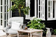 a summer Nordic terrace with rattan furniture, cozy neutral upholstery, potted greenery and a large tree