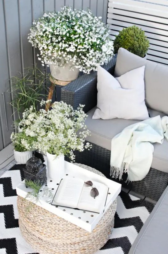 a summer Scandinavian terrace in black and white, with dark furniture, blooms and greenery in pots and a cool ottoman