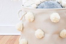 a tan fabric basket with white pompoms and white rope handles is a stylish storage piece to rock
