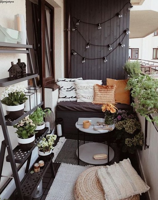 a tiny monochromatic balcony with black and white walls, blakc furniture, potted greenery and blooms and various pillows and rugs