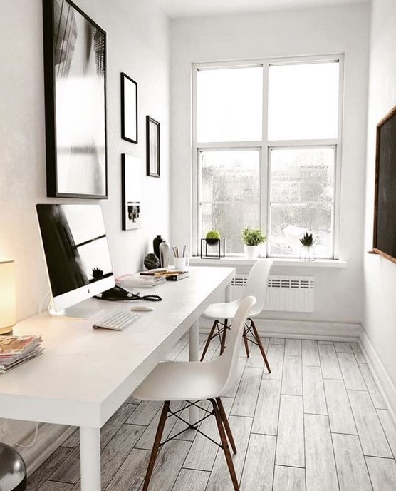 a very neutral and small home office with a shared white desk, white chairs, a gallery wall with art in black frames