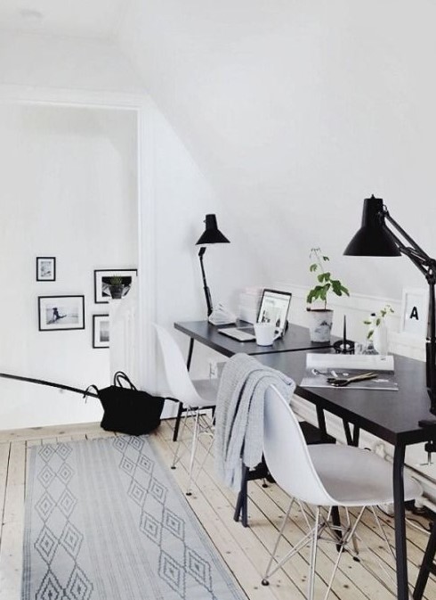 a welcoming Scandinavian space with a black desk and white chairs, black lamps and printed rugs