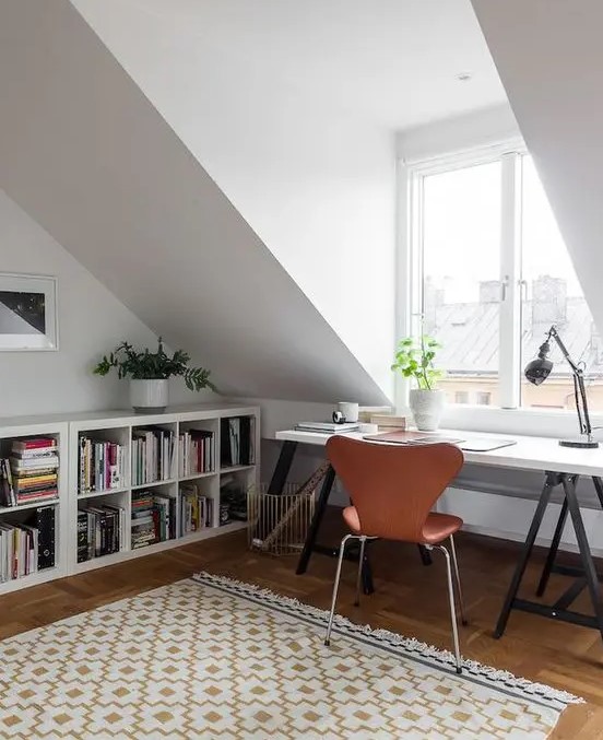 a welcoming attic home office with open bookshelves, a trestle desk, an amber leather chair and a vintage table lamp is cool