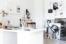 a white Nordic home office with a large white desk, a stained chair, lots of black and white artwork and a table lamp