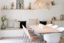 an airy Scandinavian dining space with a sleek storage bench, a light-stained table, matching white chairs, plywood pendant lamps