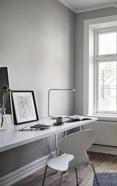 an airy Scandinavian home office with a shared desk, a white chair, black and white artworks and a table lamp