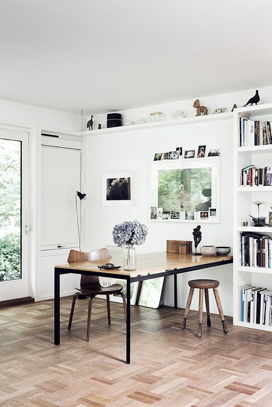 an airy Scandinavian home office with open shelving, a wooden and blackened metal desk and wooden chairs, art and photos