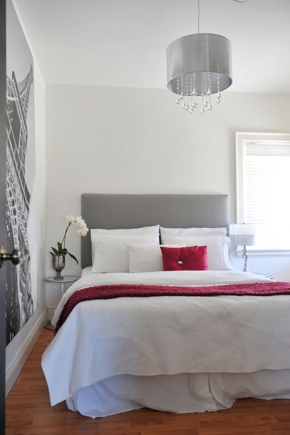 an airy bedroom with a wall mural, a grey bed with white and deep red bedding, a grey and crystal pendant lamp is amazing