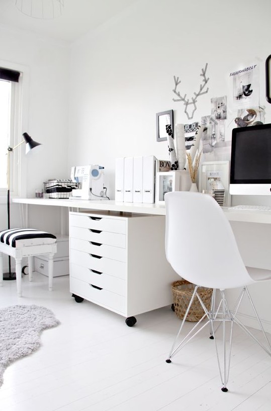an eclectic black and white home office with white furniture, a black lamp, frames for artworks and a stool with a striped seat