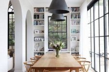 an elegant Scandinavian dining room with a stained table and chairs, built-in shelves and much natural light through the windows