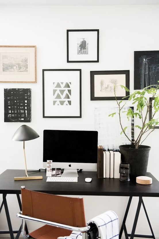 an elegant Scandinavian home office with a black trestle desk, a leather chair and a black and white gallery wall