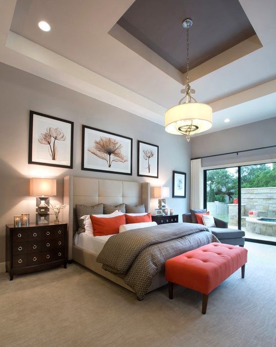 an elegant grey bedroom with a catchy ceiling, a grey upholstered wingback bed, grey and red bedding, a red upholstered bench and some black dressers as nightstands