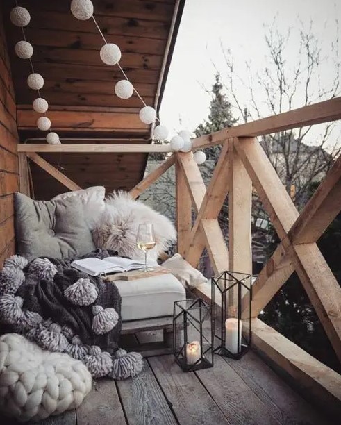 candle lanterns, lights garlands, a seat with fluffy pillows and tassel blanket for a Scandinavian balcony or terrace look