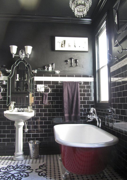 a Gothic bathroom with black walls and glossy black tiles, a fuchsia-colored tub, a free-standing sink, a chic mirror and a crystal chandelier