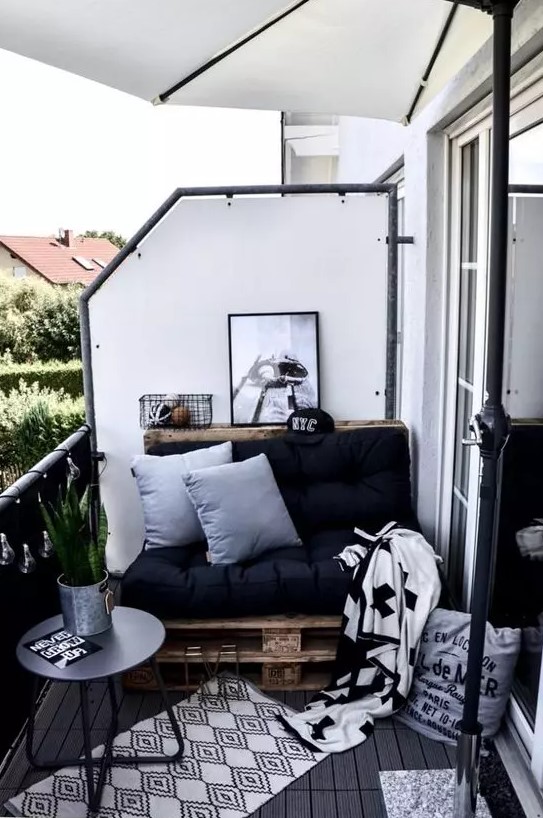 a Nordic balcony with a pallet loveseat with black upholstery, printed rugs and blankets, a black side table and a succulent