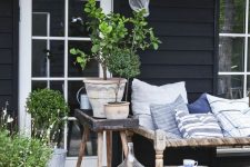a Nordic back porch with a wood and twine daybed with printed pillows, a couple of side tables and potted greenery and blooms