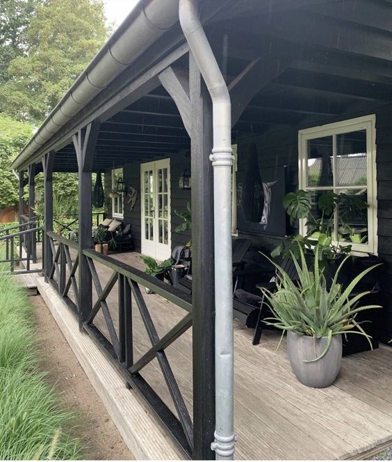 a Nordic porch with black wooden chairs, potted greenery and black loungers in the second part of the porch