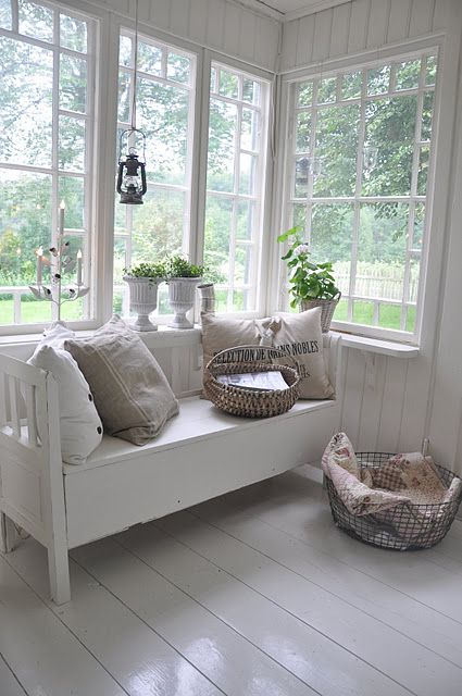 a Nordic sunroom done completely in white, with a vintage white daybed, potted plants and baskets for storage