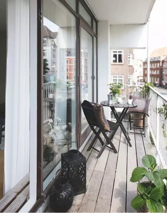 a Scandinavian balcony with black folding chairs and a table, black candle lanterns, potted greenery and blooms