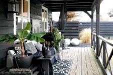 a Scandinavian porch with a black daybed with black and white pillows, a side table with black vases, potted plants and lanterns
