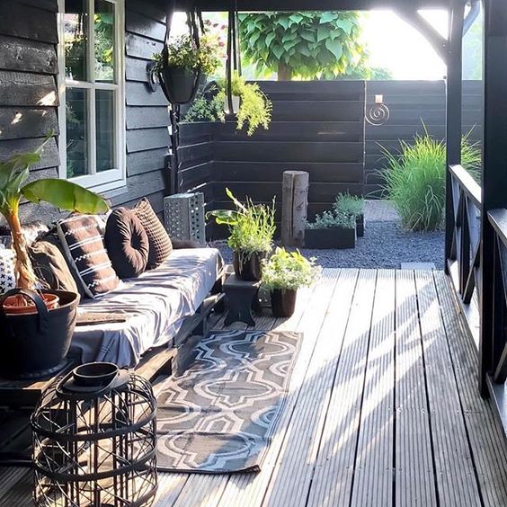 a Scandinavian porch with a pallet sofa with printed pillows and upholstery, a large candle lantern and potted greenery