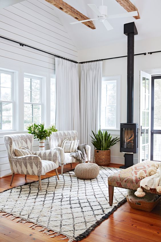 a Scandinavian sunroom and living room with white planked walls and a ceiling, with printed chairs and a daybed, a metal hearth and some greenery