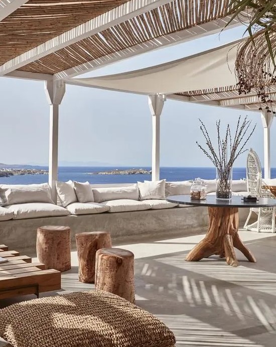 a beach patio with a concrete bench, neutral upholstery, wooden and woven furniture and accessories and a beautiful sea view
