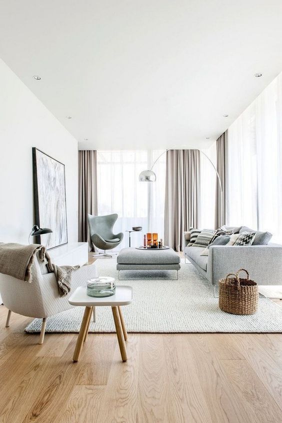 a beautiful contemporary living room with grey and creamy seating furniture, printed pillows, a side table, grey curtains and a basket
