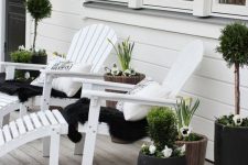 a black and white Scandinavian porch with white loungers, black and white upholstery, potted greenery and blooms