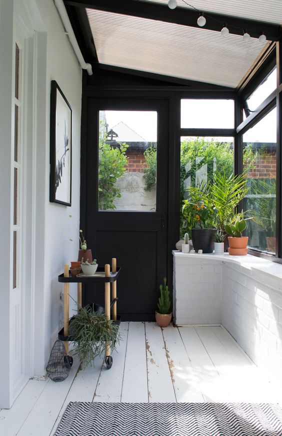 a black and white Scandinavian sunroom with a glass ceiling, lights and lots of greenery to make it double as an orangery