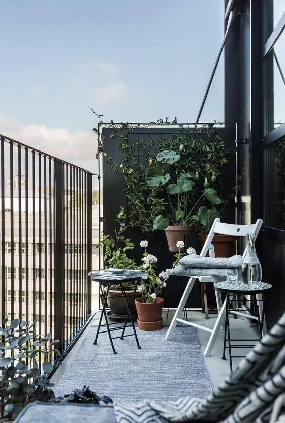 a black balcony done with a couple of folding chairs and a small coffee table plus a lot of greenery around