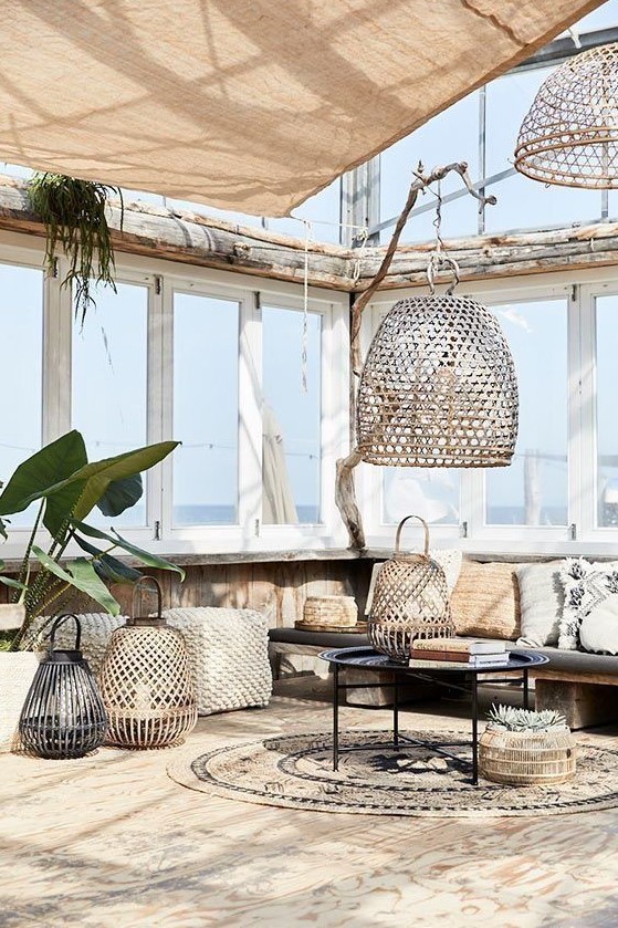 a boho chic tropical patio with a large upholstered bench, rattan and metal lanterns and a boho rug plus potted greenery