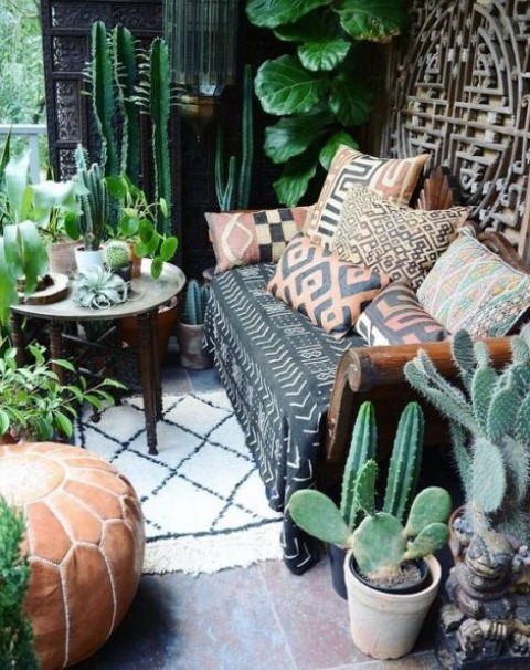 a boho desert terrace with cacti, greenery, statement plants, a sofa with printed pillows and a carved wooden table
