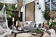 a boho patio with a jute rug and poufs, a sofa with black and white pillows, a low black table and a pendant chair