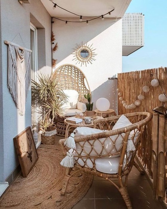 a boho summer balcony with a jute rug, rattan furniture, lamps, an artwork, macrame and potted plants is beautiful and welcoming