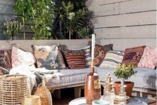 a boho terrace with an L-shaped bench, woven lanterns, a small coffee table, printed pillows and lots of greenery