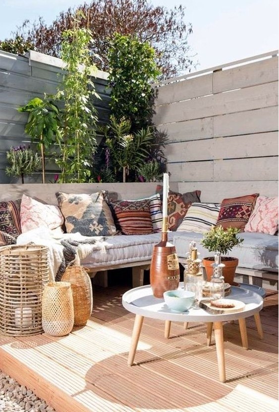 a boho terrace with an L-shaped bench, woven lanterns, a small coffee table, printed pillows and lots of greenery