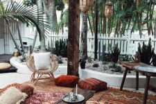 a boho terrace with colorful layered rugs, bright cushions and pillows, a rattan chair, Moroccan lanterns and cacti all around