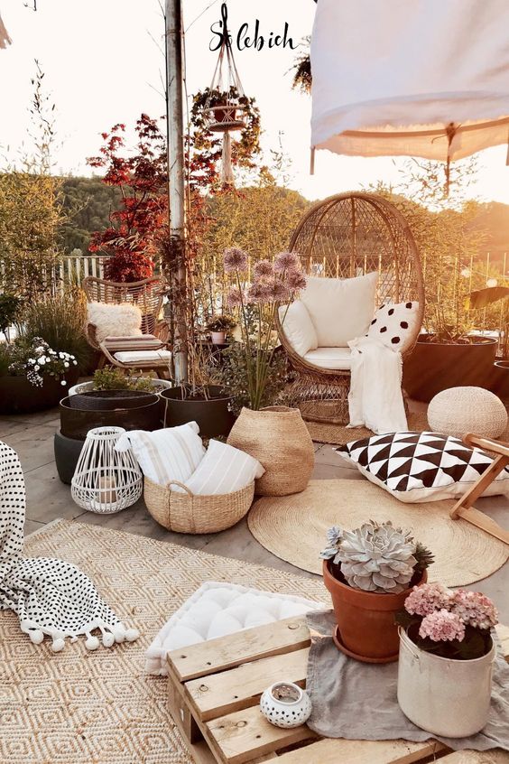 a boho terrace with jute rugs, a wicker egg-shaped chair, potted plants and blooms, candle lanterns and an umbrella