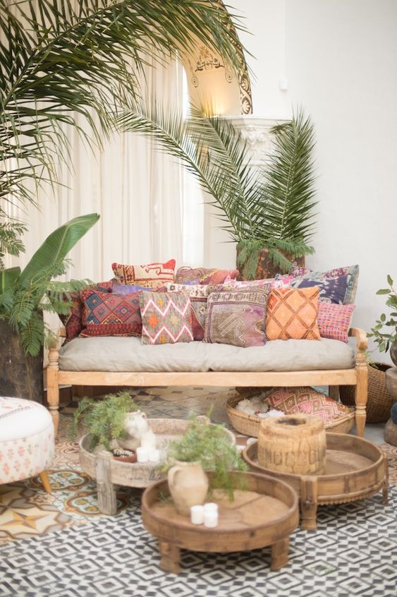 a boho terrace with light-stained furniture, colorful printed pillows, low coffee tables, potted greenery and candles