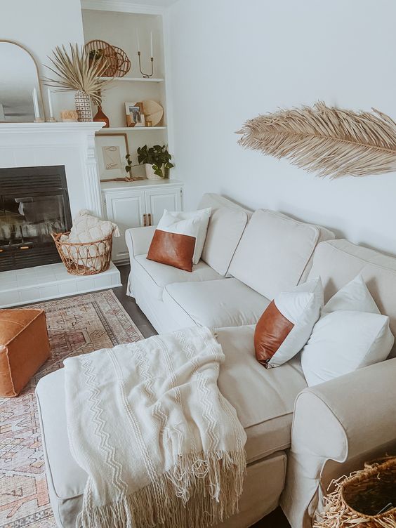 a boho tropical neutral living room with built in storage units and shelves, a built in fireplace, a white sectional, brown and amber leather accents
