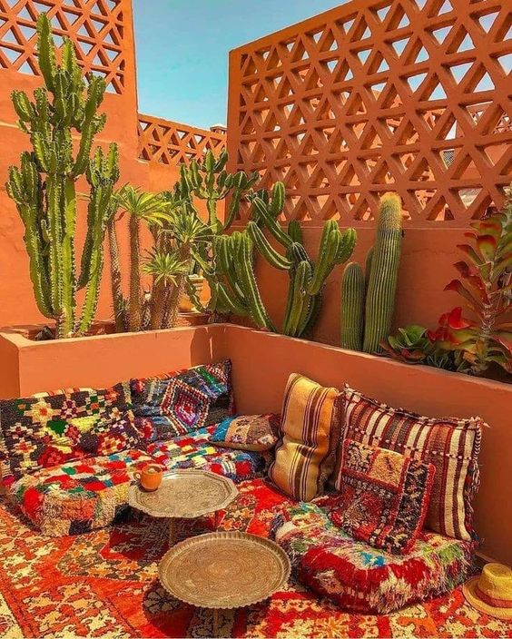 a bold Moroccan terrace with colorful rugs and cushions, low coffee tables and large cacti growing there