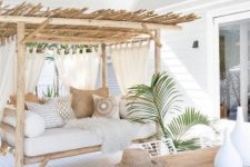 a breezy and airy tropical terrace done in neutrals with wooden furniture, printed pillows, some greenery