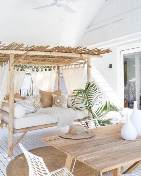 a breezy and airy tropical terrace done in neutrals with wooden furniture, printed pillows, some greenery